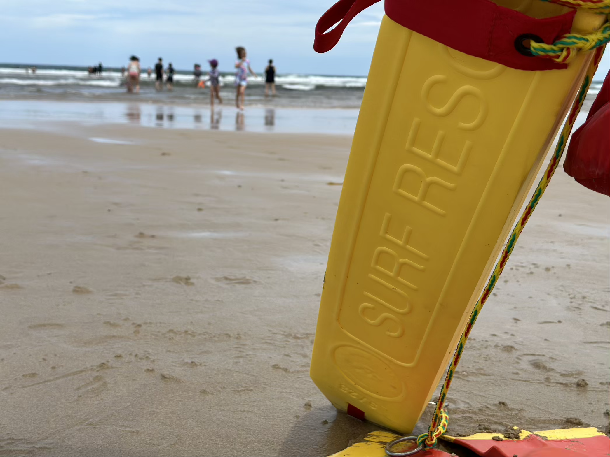 Yellow surfrider rescue board on beach with people in background